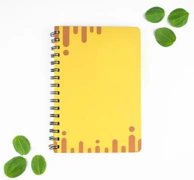 A single yellow colored diary with green leaves as a border before a paper ba Stock Photos