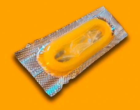 SINGLE YELLOW CONDOM IN FOIL WRAPPER ON YELLOW BACKGROUND Stock Photos