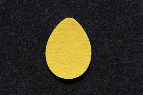Single yellow felt egg shape against dark grey felt background Stock Photos