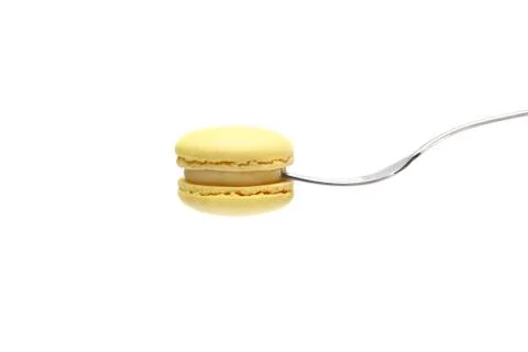 Single yellow macaron or macaroon cake on a fork on white background. side vi Stock Photos
