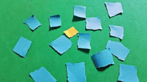 Single yellow paper square surrounded by many blue paper scraps Stock Photos