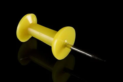 Single yellow pushpin with sharp metal point on a reflective black surface Stock Photos