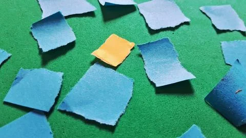 Single yellow torn paper square centered among many blue pieces Stock Photos