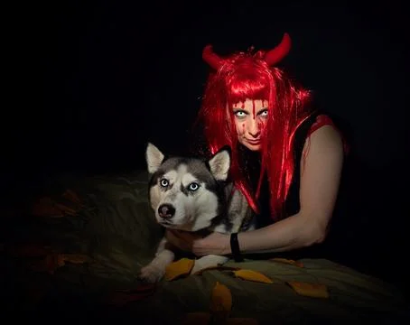 Sinister Devil Woman Hugging Husky Dog in Dark Halloween Scene Stock Photos