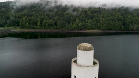 Sinking drone revealing tower in water reservoir with black water and trees  Stock Footage 251658248