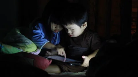 Sister and brother using touch pad lying in bed at night. Bright screen lighting 스톡 동영상 55420283