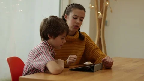 Sister And Younger Brother Using Tablet Together At Wooded Dinning Table Stock Footage 101199194