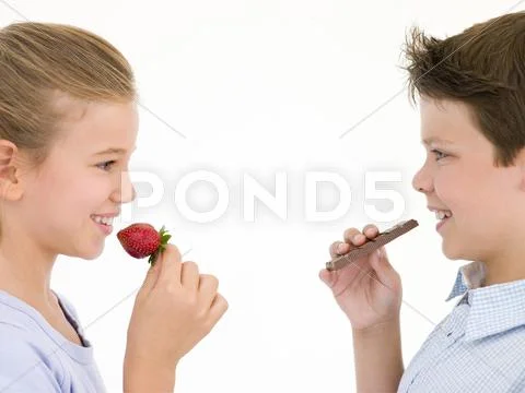 Sister eating strawberry by brother eating chocolate bar Stock Photos