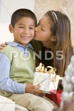 Sister Giving Her Brother A Christmas Present And Kissing Him On The Cheek Stock-Fotos