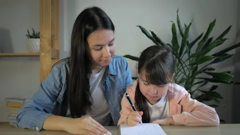 Sister or young mom help little girl make homework. Girls sitting at the table Stock Footage 165779367