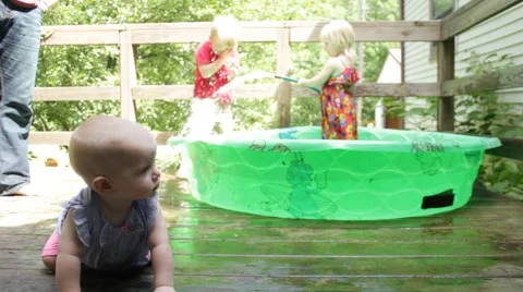 Sister sprays brother in background while baby crawls in foreground Stock Footage 40028482