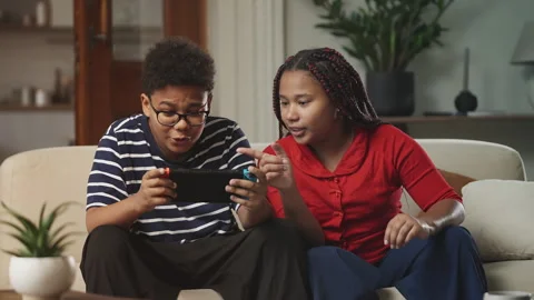 Sister talking to her brother while playing video games together at home Video stock 337090154