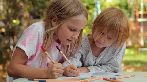 Sister teaching younger sibling to write in a notebook while sitting at an .. Stock Footage 304327680