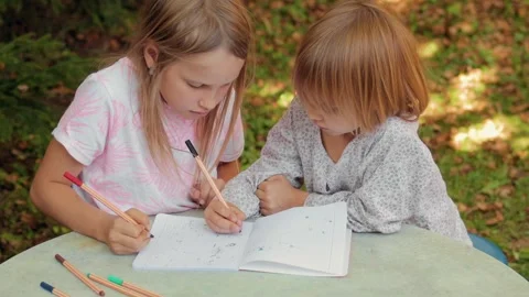 Sister teaching younger sibling to write in a notebook while sitting at an .. Stock Footage 304327770