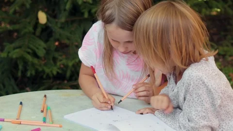 Sister teaching younger sibling to write in a notebook while sitting at an .. Stock Footage 304328036