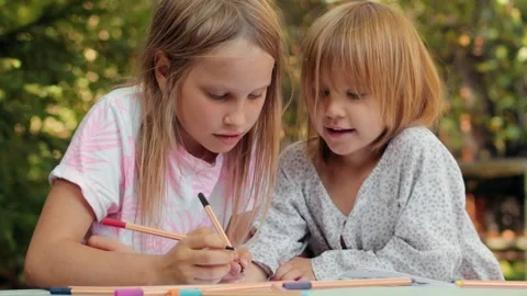 Sister teaching younger sibling to write in a notebook while sitting at an .. Stock Footage 304328037