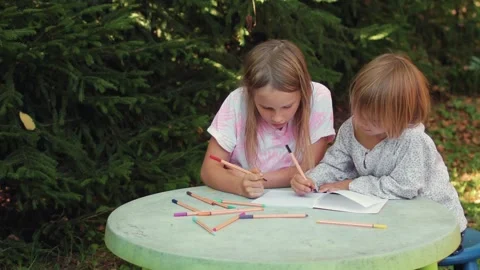 Sister teaching younger sibling to write in a notebook while sitting at an .. Stock Footage 304328049