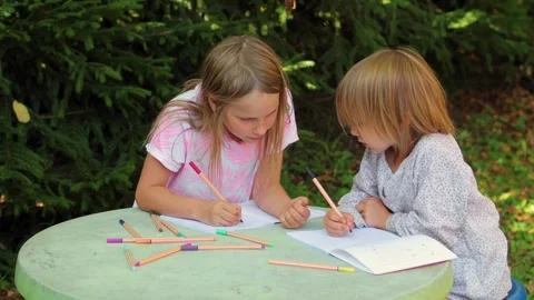 Sister teaching younger sibling to write in a notebook while sitting at an .. Stock Footage 304328303