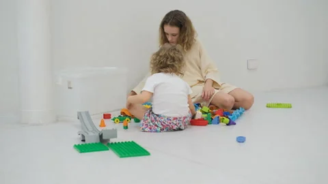 Sisters assembling colorful blocks on the floor Видео 335425084