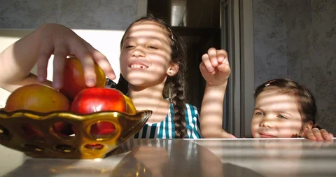 Sisters getting out from under  table and taking apples from plate 스톡 동영상 128025400