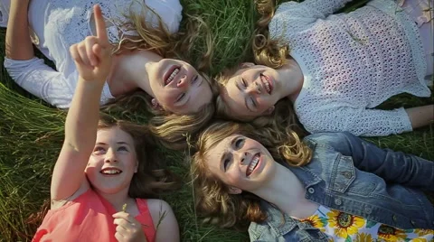 Sisters Lay In Grass, Youngest Points At Sky, They All Look Up Excitedly Video stock 42906632