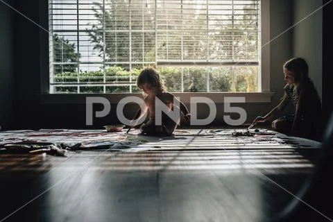 Sisters painting while sitting on floor against window at home Stock Photos