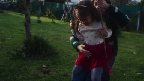 Sisters play happily swinging on a tree in sunny backyard afternoon Stock Footage 320028862