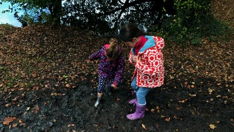 Sisters playing in a muddy puddle Stock Footage 99374821