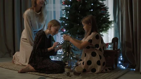 The sisters sit under the Christmas tree and decorate a small tree with cones. 스톡 동영상 143515020