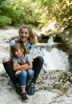 Sisters sitting on rocks next to a river. Stock Photos