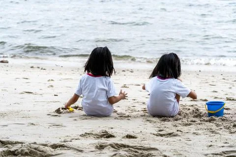 Sisters while sitting on the sand and playing with sand and beach toys Stock Photos