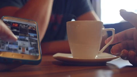 Sit in a cafe for a cup of coffee and leaf through the photos in the phone. 4k Stock Footage 88775405