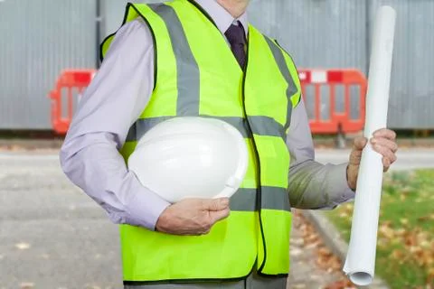 Site engineer in high visibility vest holding drawings and hard hat Stock Photos
