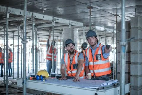 Site foreman and builder pointing from blueprint in construction site 스톡 사진