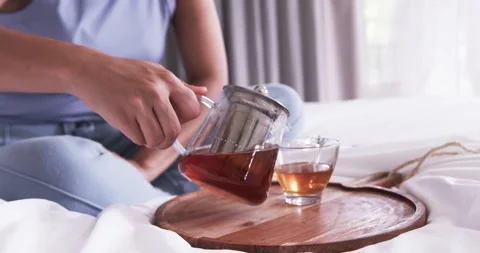Sitter is reaching for teapot, lifting and tilting it on tray on bed to fill cup Stock Footage 344645268
