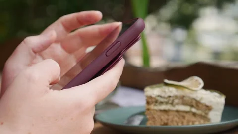 Sitting at a cafe table, a woman scrolls on her smartphone beside coffee and Video stock 323809639