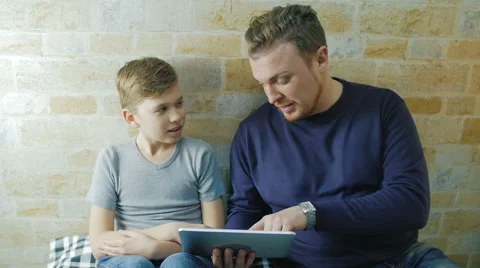 Sitting on the couch with a man and his son watching something on the plate Stock Footage 62066675