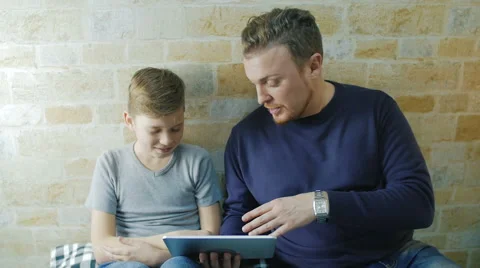 Sitting on the couch with a man and his son watching something on the plate Stock Footage 62066685