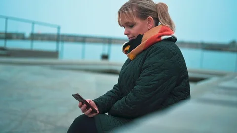 Sitting down and using mobile phone in cold weather next to the sea Stock Footage 122258453