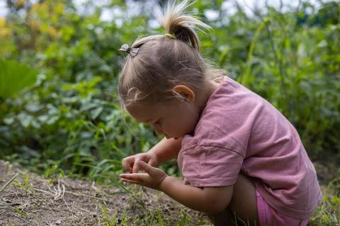 Sitting down, the child examines a small insect on his hand. Cute child girl Foto stock