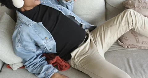 Sitting down on sofa edge, middle-aged man in denim jacket sliding, putting on Stock Footage 337704932