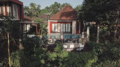 Sitting on the edge of the pool next to the summer villa aerial footage Stock Footage 100273663