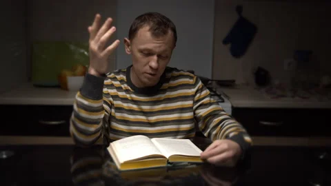 Sitting in the evening at the table, a man with an expression reads text Stock Footage 131142316