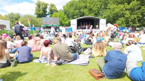 Sitting on field at the Cambridge pride after party as an act performs on stage Stock Footage 338018056