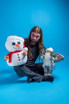 Sitting long haired man while holding a Santa Claus and a snowman toy and Stock Photos