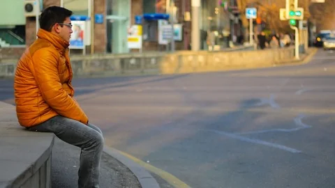 Sitting man in an orange jacket with thoughtful look, on the background of Time Vidéo 83636332