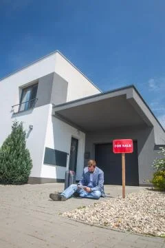 Sitting man without work in front of the house during economic crisis, selling 库存照片