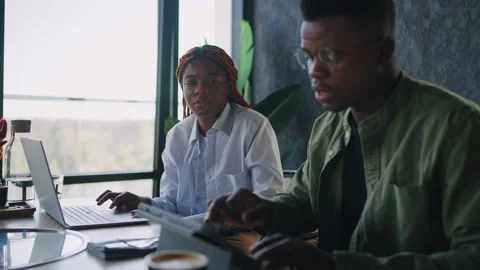 Sitting next to a laptop at a cafe, two black business partners - a male and a Stock Footage 239268416