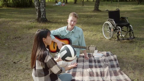 Sitting on the plaid in the public park, a disabled young man offers his Stock Footage 174497801
