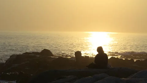 Sitting on the rocks overlooking a golden sunset near the ocean Stock Footage 337543011